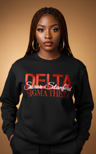 Load image into Gallery viewer, Woman wearing a black sweatshirt with 'Delta Sigma Theta' text on a brown background
