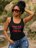 A woman wearing a black tank top with 'DELTA SIGMA THETA' printed in red and white script, paired with blue jeans and red-tinted sunglasses, standing outdoors near a stream and rocks.